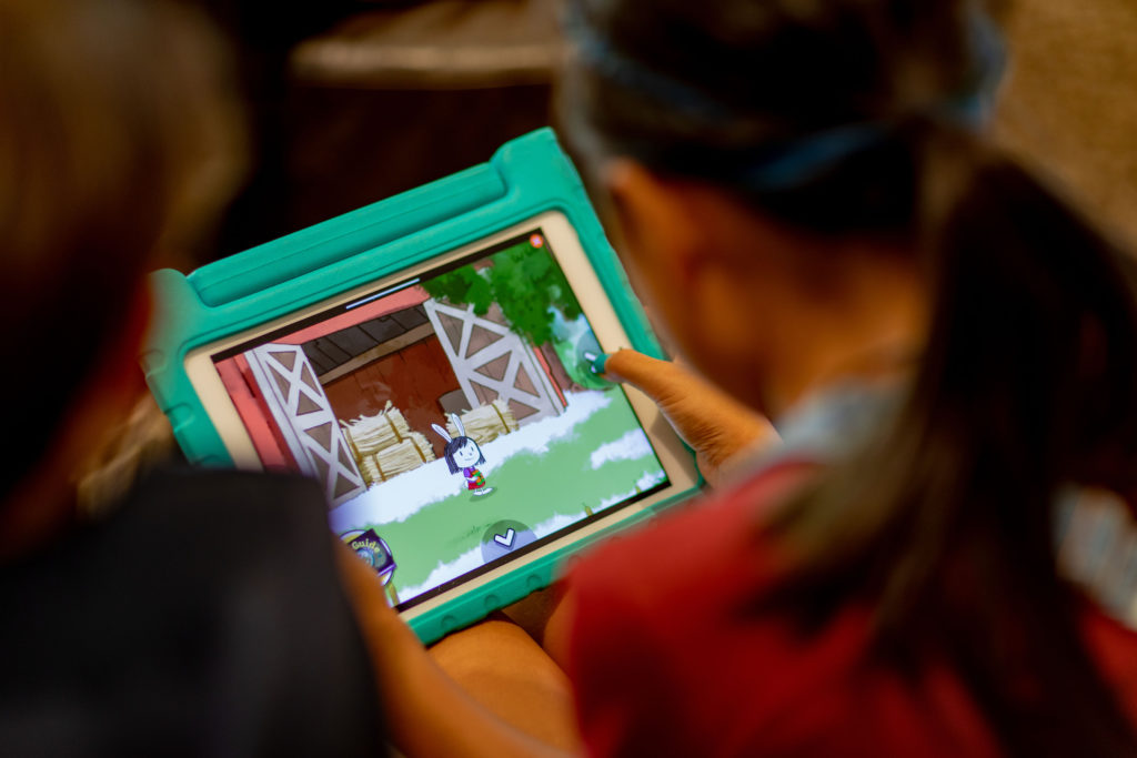 Over the shoulder view of girl with ponytail playing on her tablet. Did you know your kids can play while learning in Roblox?