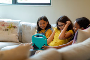 Help your kids find the best learning apps they'll love to play. Three young girls sitting and smiling on a couch together playing on a tablet.
