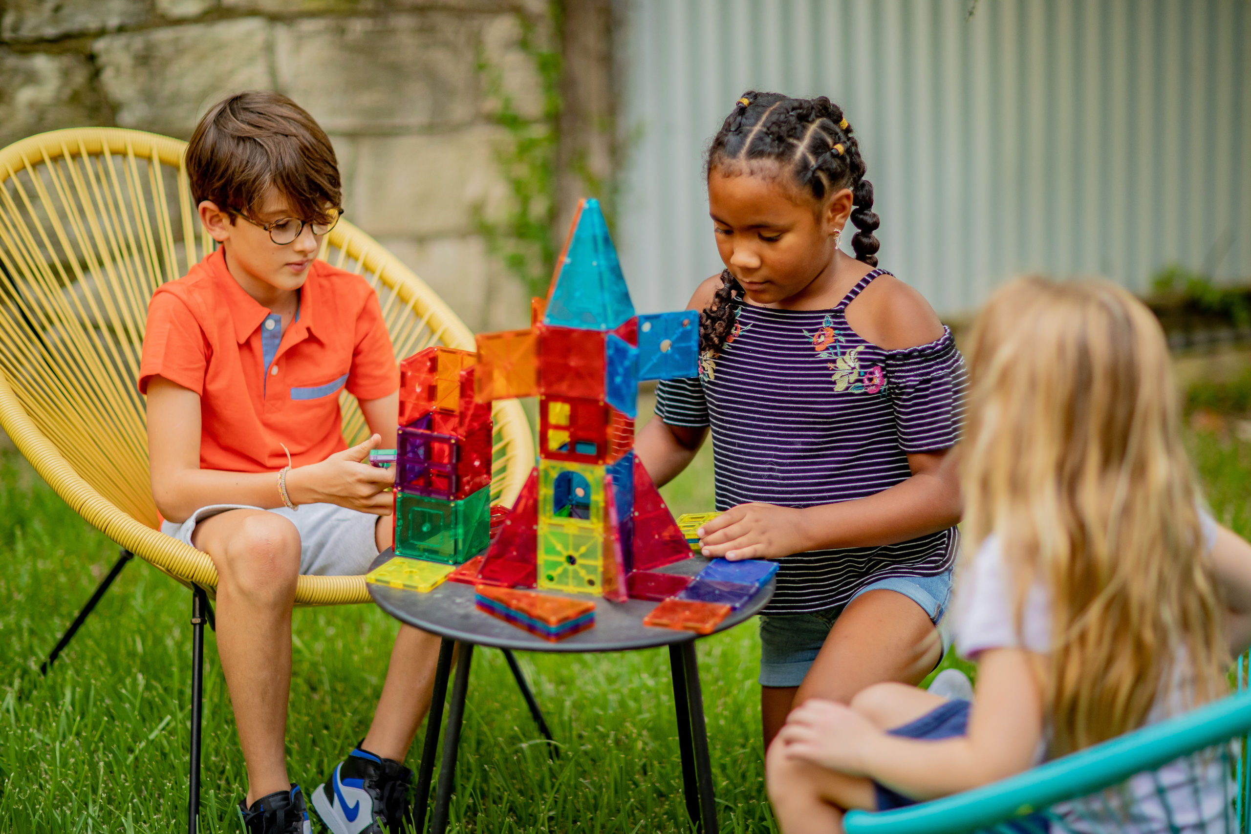 Three kids sitting outside building a castle with colorful plastic panels. Hands-on STEM activities are a great way to practice tech concepts without screens.