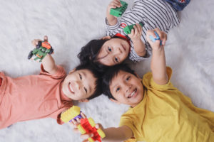 3 kids laying down and looking up at the camera holding their favorite toys and looking happy. When kids are granted more autonomy to live and play as they'd like, they're more likely to thrive.