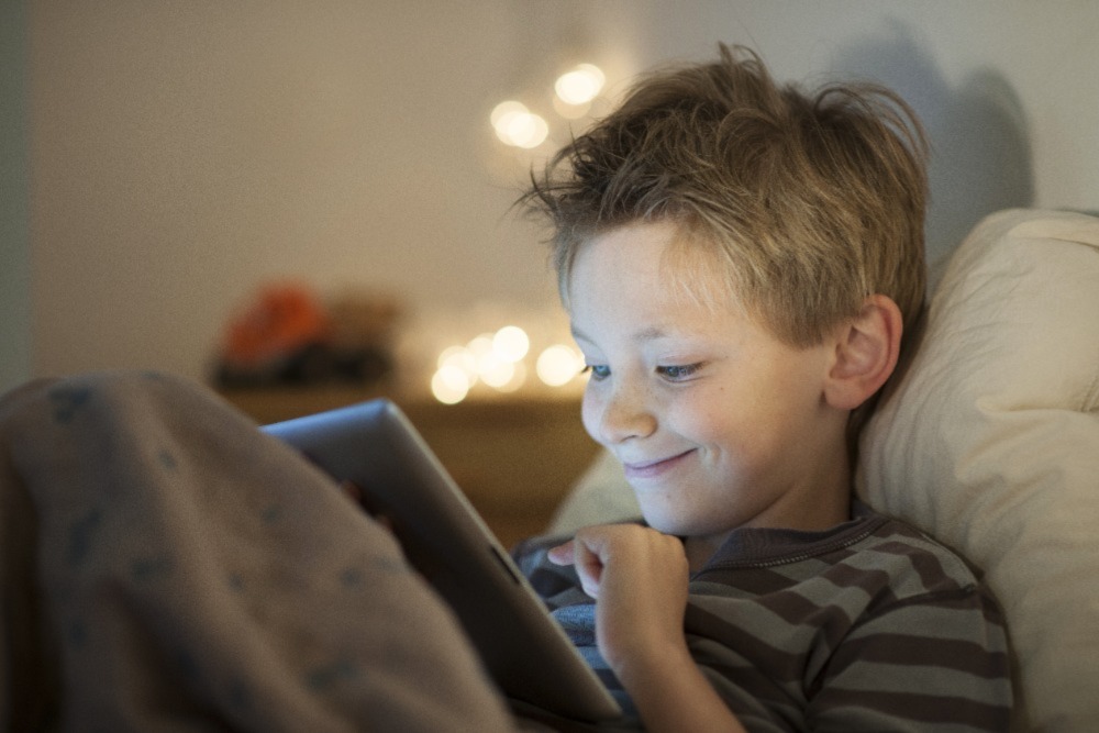 Young boy smiling while playing a Roblox horror game on his tablet.