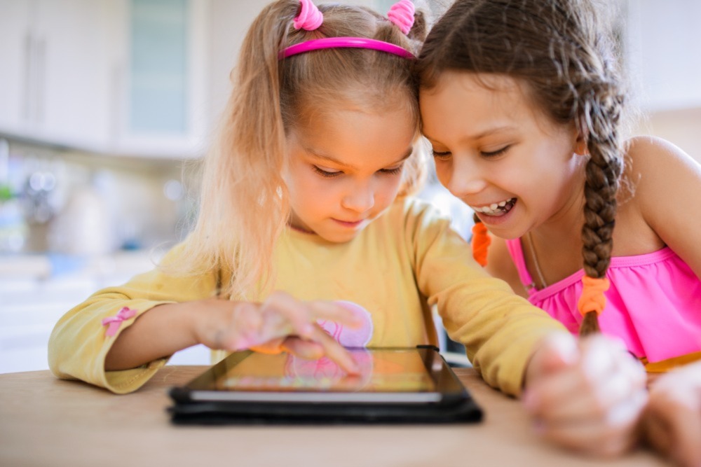 Two young girls smiling big while enjoying screen time together on a tablet. Possibly playing roguelike games - but based on their smiles, probably not.
