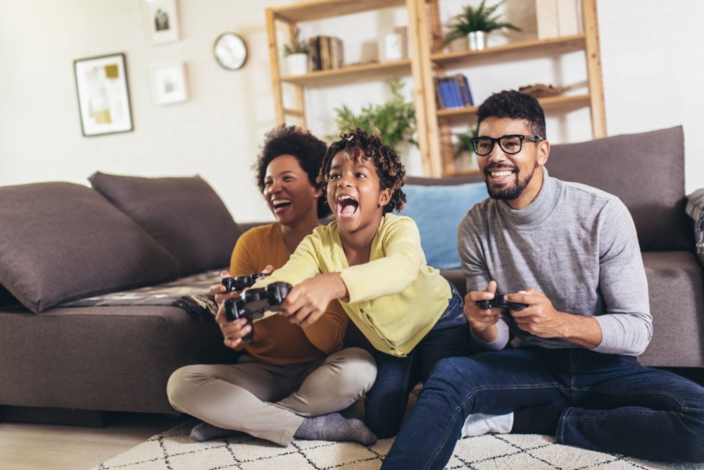 A family is playing video games, laughing and smiling while sitting together on their couch. This is one way to enjoy Gameschooling.