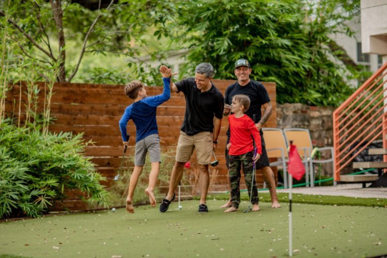 Two dads with their kids celebrating after sinking a putt. Games of all kinds bring more fun to learning with gameschooling.