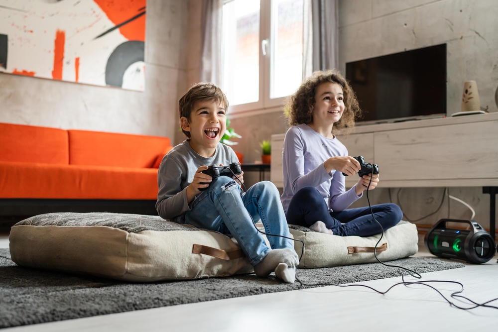 Two kids sitting on pillows on the floor playing video games together.
