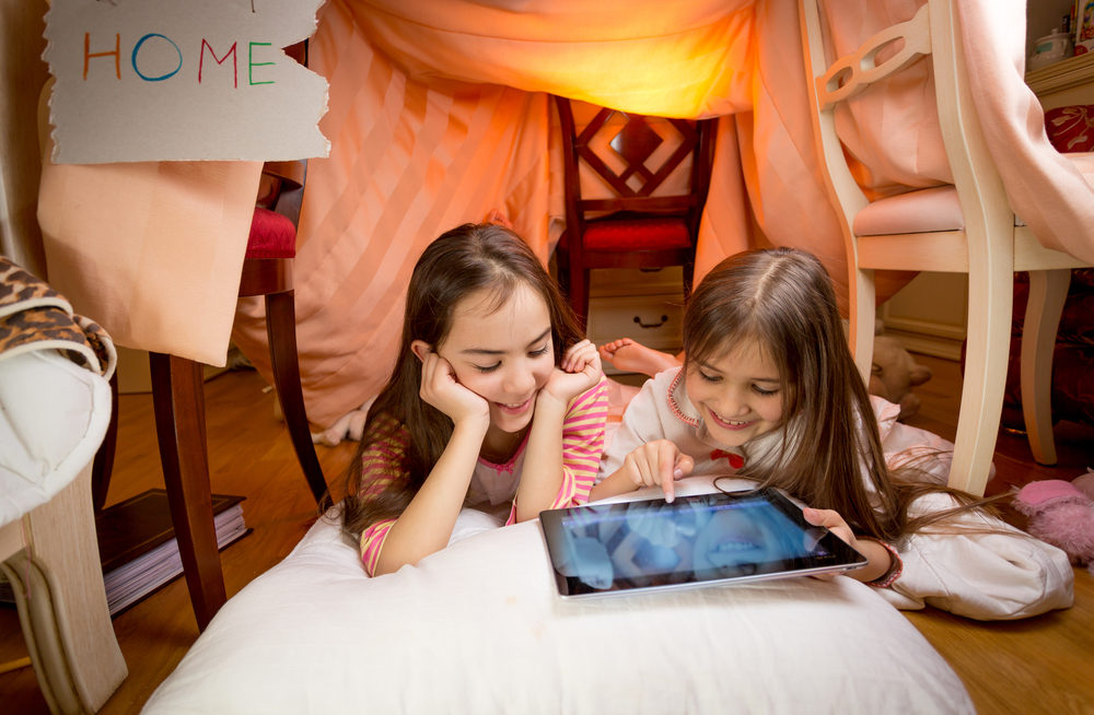 2 young girls under a blanket looking at a tablet. Did you know video games count as gameschooling?