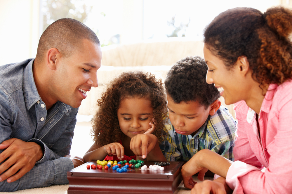 A mom, dad and two kids playing a board game. Board games are a classic gameschooling resource.